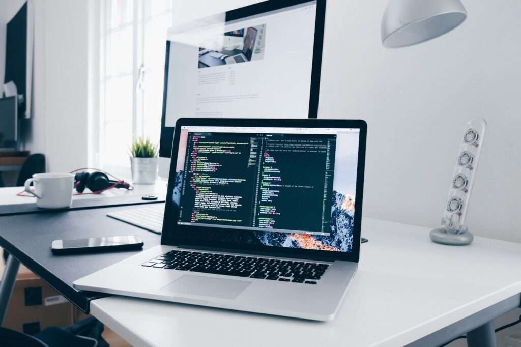 A macbook with lines of code on its screen on a busy desk